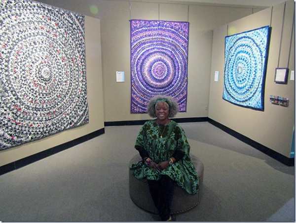 Betty Ford-Smith in front of an exhibition of several of the Pine Cone/Pine Burr quilts she made.